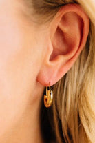 Close-up of a person wearing gold hoop earrings with blonde hair.
