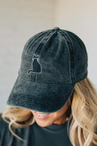 Person wearing a dark gray cap with a cat emblem on a neutral background