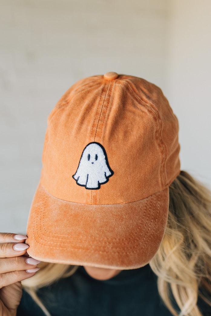 Orange cap with a ghost design held by a person against a neutral background
