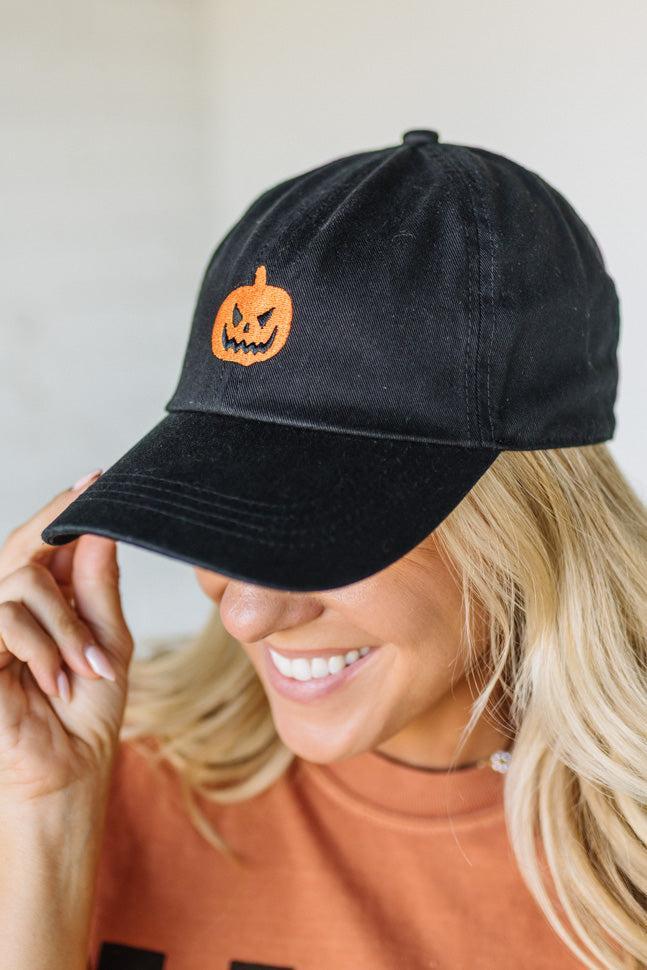 Black cap with a pumpkin design worn by a person against a neutral background