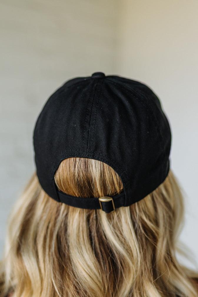 Black cap worn by a person with blonde hair against a neutral background