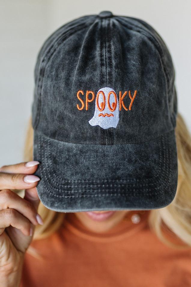 Black distressed cap with 'SPooky' and ghost design held by a person wearing an orange shirt.