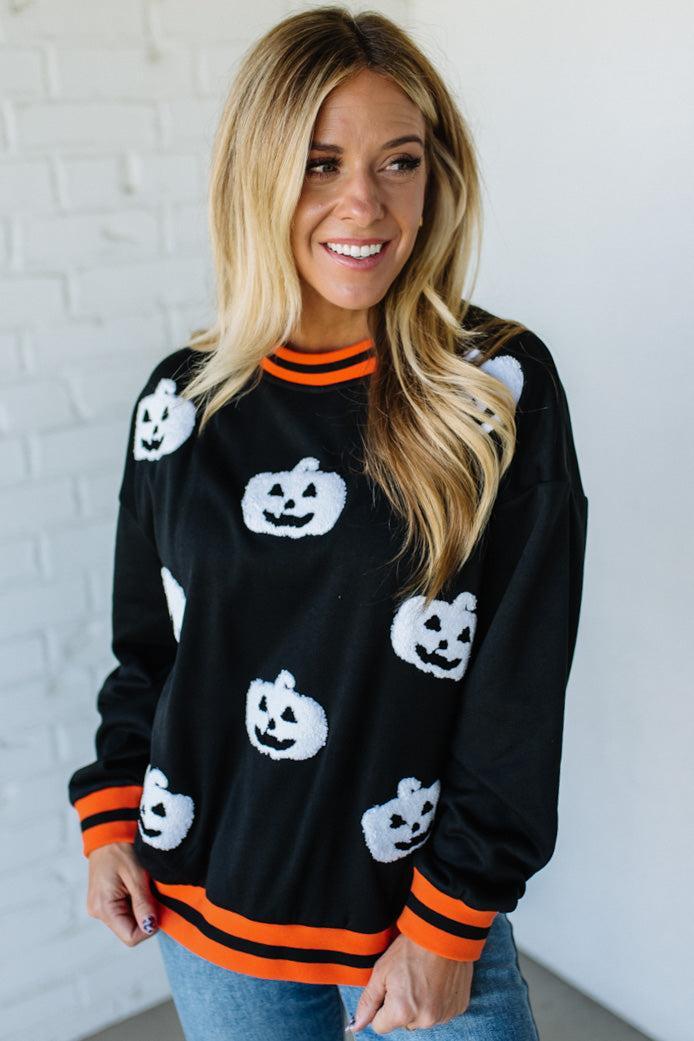 Woman wearing a black sweater with white pumpkin designs against a white brick wall.
