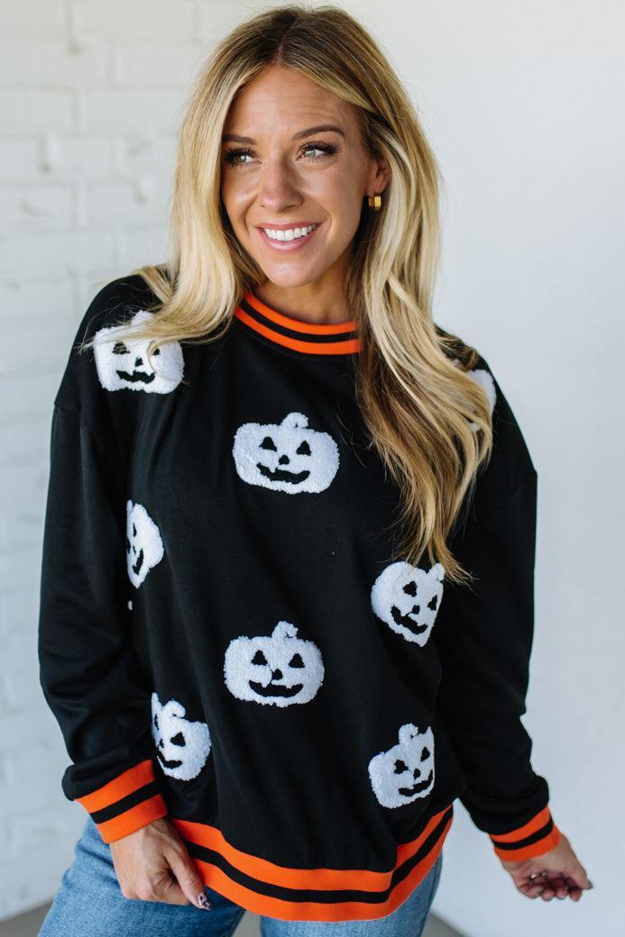 Woman wearing a black Halloween sweater with white jack-o'-lantern designs and orange trim.