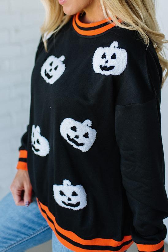 Black sweater with white pumpkin faces and orange accents worn by a person.