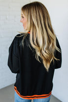 Woman wearing a black jacket with orange accents against a white wall