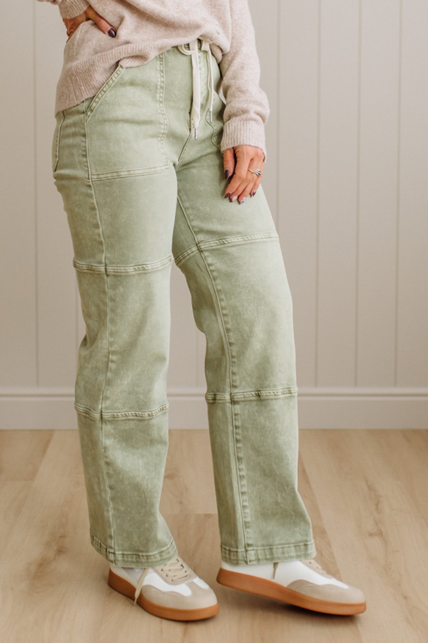 Person wearing light green jeans and white shoes on a wooden floor.