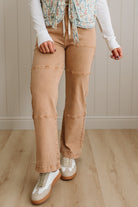 Person wearing beige pants and a floral top in a room with wooden flooring and a neutral wall.