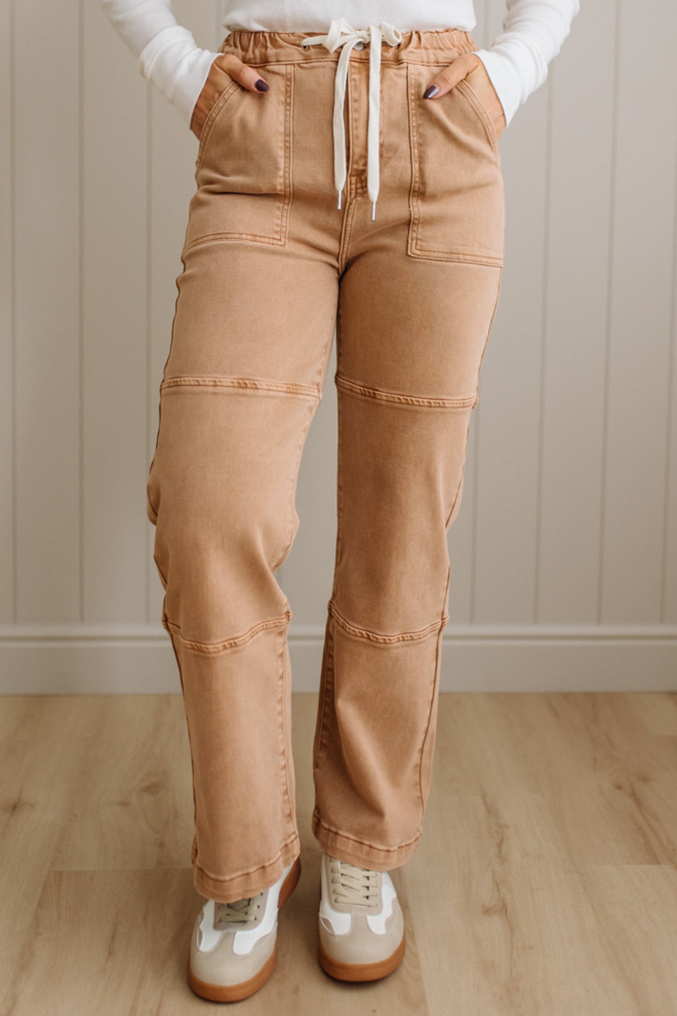 Person wearing tan pants and white sneakers in a room with wooden flooring and a neutral wall.