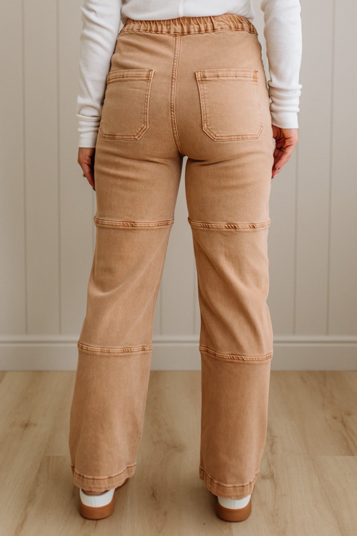 Person wearing tan pants with a white shirt in a minimal indoor setting