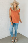 Woman wearing a solid rust colored gauze top with a short ruffle sleeve
