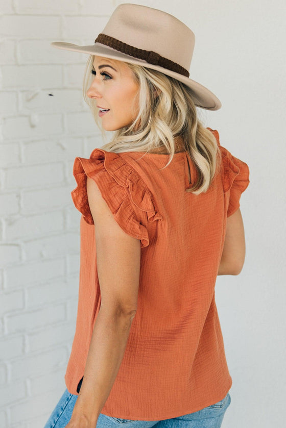 Woman wearing a solid rust colored gauze top with a short ruffle sleeve
