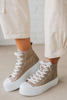 Beige high-top sneakers with white laces and soles worn with light-colored pants on a neutral background.