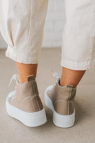 Beige sneakers with white soles worn with light-colored pants on a neutral background