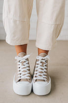 Person wearing beige high-top sneakers with white laces on a neutral background