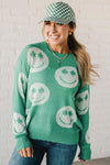 BLONDE WOMEN IN A GREEN AND WHITE CHECKER HAT WEARING A GREEN AND WHITE LOW GAUGE SWEATER WITH SMILEY WITH SHAMROCK EYES PATTERN.