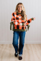 Blonde woman wearing a orange, brown and cream check sweater with olive green ribbed trim and bows at the elbow.