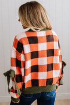 Blonde woman wearing a orange, brown and cream check sweater with olive green ribbed trim and bows at the elbow.
