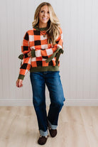 Blonde woman wearing a orange, brown and cream check sweater with olive green ribbed trim and bows at the elbow.