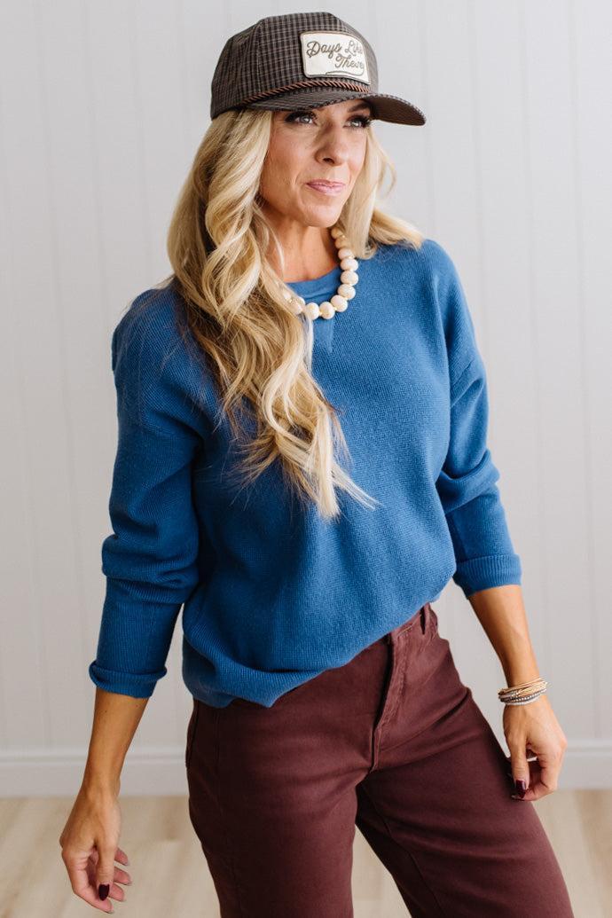 Blonde woman in a plaid hat wearing a solid waffle texture sweater with drop shoulder seams and crewneck.