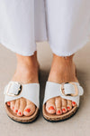 Cork sole sandals with white faux leather straps and gold buckle accent.