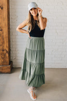Blonde woman wearing a spruce green tiered rayon maxi skirt with elastic waistband.