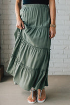 Blonde woman wearing a spruce green tiered rayon maxi skirt with elastic waistband.