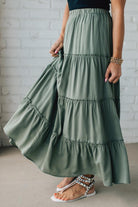 Blonde woman wearing a spruce green tiered rayon maxi skirt with elastic waistband.