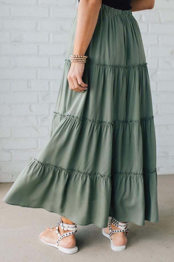Blonde woman wearing a spruce green tiered rayon maxi skirt with elastic waistband.