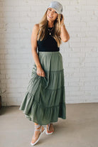 Blonde woman wearing a spruce green tiered rayon maxi skirt with elastic waistband.