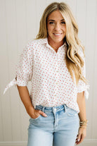 Woman wearing a white blouse with red mini heart patterns and light blue jeans against a neutral background