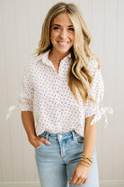 Woman wearing a white blouse with red mini heart patterns and light blue jeans against a neutral background