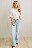 Woman wearing a white blouse with rolled-up sleeves and light blue jeans against a white paneled wall.