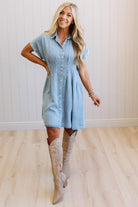 Woman wearing a light blue dress and beige knee-high boots indoors.