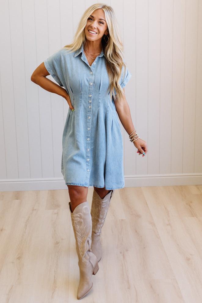Woman wearing a light blue dress and beige knee-high boots indoors.