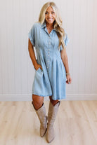 Woman wearing a light blue dress and beige boots against a white wall.