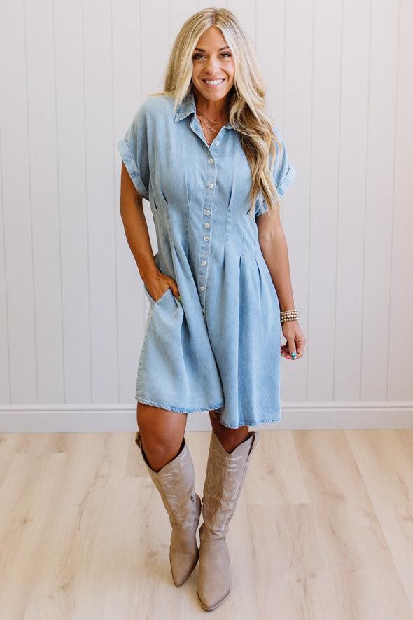 Woman wearing a light blue dress and beige boots against a white wall.