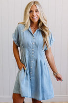 Woman wearing a light blue denim dress against a white wall.