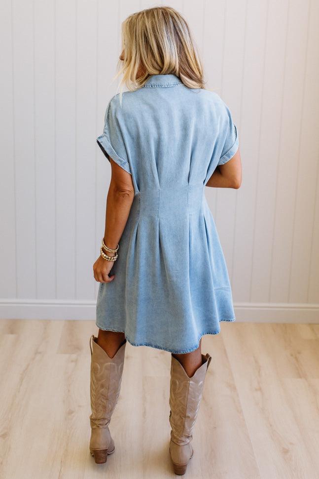 Woman wearing a light blue dress and beige boots in a room with wooden flooring.