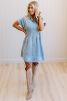Woman wearing a light blue denim dress and beige cowboy boots indoors.