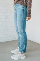 Person wearing light blue jeans and white sneakers against a white brick wall.