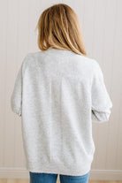 BLONDE WOMAN WEARING A HIGH-LOW HEM, LONG SLEEVE, SUPER SOFT, OVERSIZED CREW NECK SWEATER WITH RIB DETAILS AND STANDING IN A STUDIO WITH LIGHT WOOD FLOOR AND PANELED WALL BEHIND.