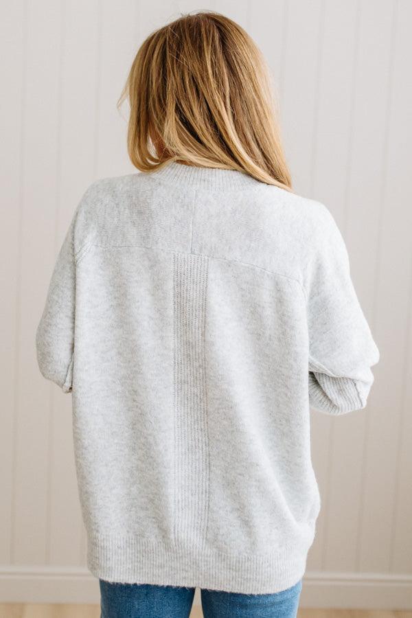 BLONDE WOMAN WEARING A HIGH-LOW HEM, LONG SLEEVE, SUPER SOFT, OVERSIZED CREW NECK SWEATER WITH RIB DETAILS AND STANDING IN A STUDIO WITH LIGHT WOOD FLOOR AND PANELED WALL BEHIND.