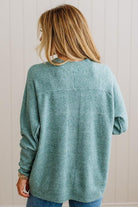 BLONDE WOMAN WEARING A HIGH-LOW HEM, LONG SLEEVE, SUPER SOFT, OVERSIZED CREW NECK SWEATER WITH RIB DETAILS AND STANDING IN A STUDIO WITH LIGHT WOOD FLOOR AND PANELED WALL BEHIND.