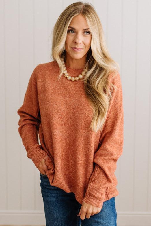 BLONDE WOMAN WEARING A HIGH-LOW HEM, LONG SLEEVE, SUPER SOFT, OVERSIZED CREW NECK SWEATER WITH RIB DETAILS AND STANDING IN A STUDIO WITH LIGHT WOOD FLOOR AND PANELED WALL BEHIND.