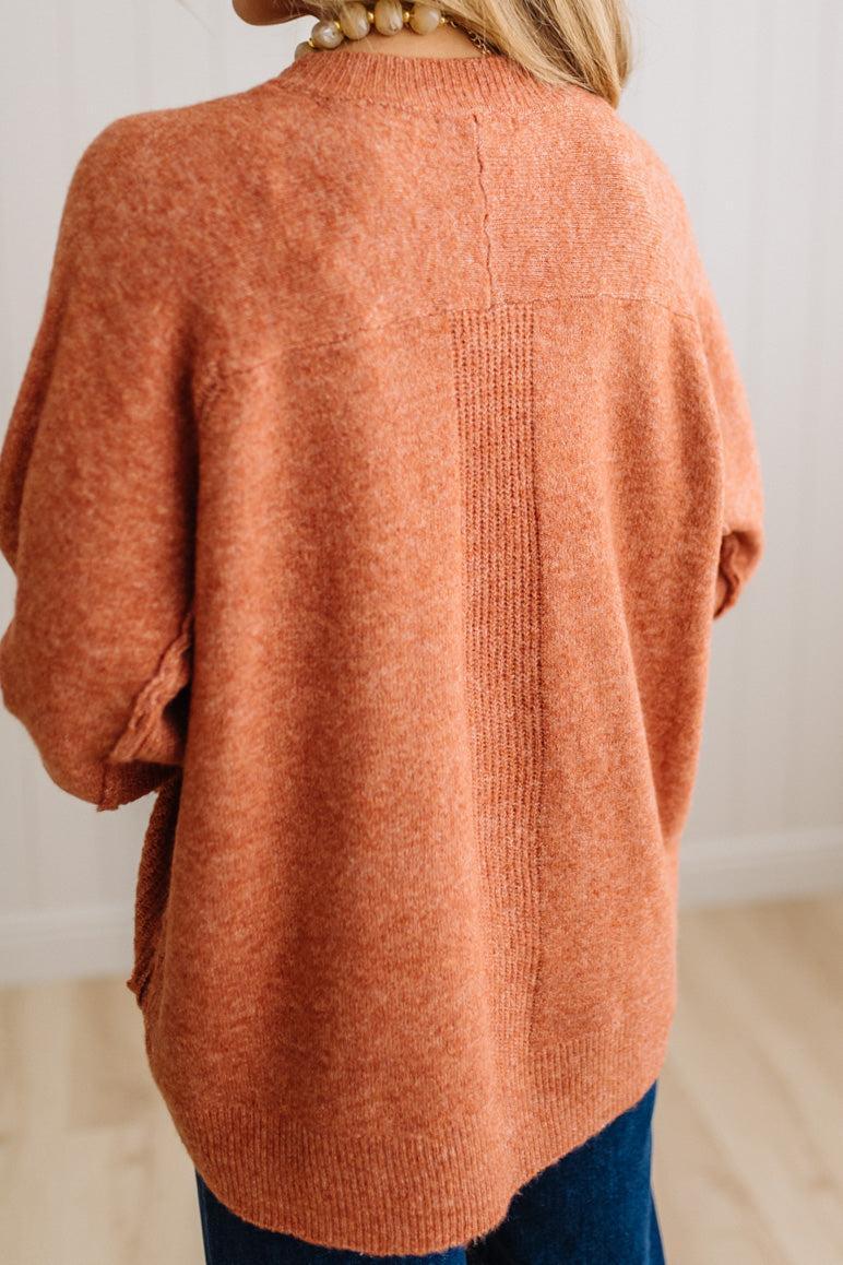 BLONDE WOMAN WEARING A HIGH-LOW HEM, LONG SLEEVE, SUPER SOFT, OVERSIZED CREW NECK SWEATER WITH RIB DETAILS AND STANDING IN A STUDIO WITH LIGHT WOOD FLOOR AND PANELED WALL BEHIND.