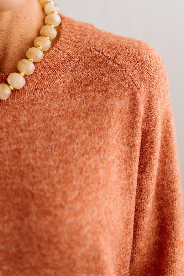 BLONDE WOMAN WEARING A HIGH-LOW HEM, LONG SLEEVE, SUPER SOFT, OVERSIZED CREW NECK SWEATER WITH RIB DETAILS AND STANDING IN A STUDIO WITH LIGHT WOOD FLOOR AND PANELED WALL BEHIND.