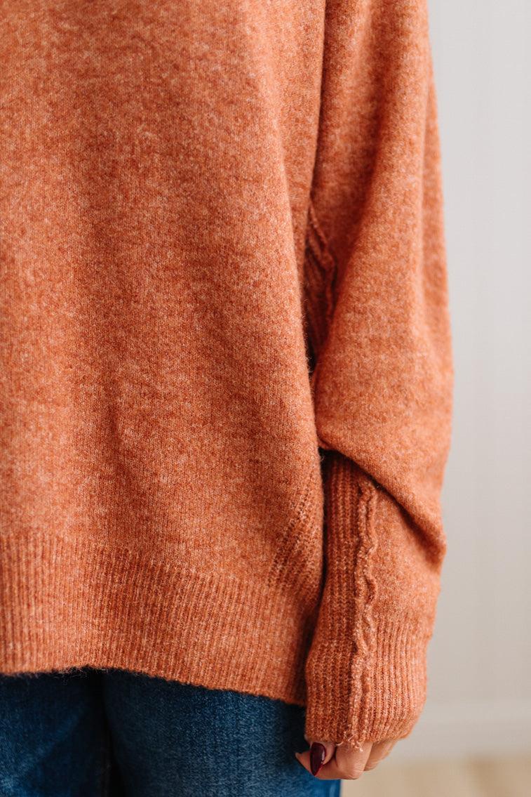 BLONDE WOMAN WEARING A HIGH-LOW HEM, LONG SLEEVE, SUPER SOFT, OVERSIZED CREW NECK SWEATER WITH RIB DETAILS AND STANDING IN A STUDIO WITH LIGHT WOOD FLOOR AND PANELED WALL BEHIND.