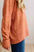 BLONDE WOMAN WEARING A HIGH-LOW HEM, LONG SLEEVE, SUPER SOFT, OVERSIZED CREW NECK SWEATER WITH RIB DETAILS AND STANDING IN A STUDIO WITH LIGHT WOOD FLOOR AND PANELED WALL BEHIND.