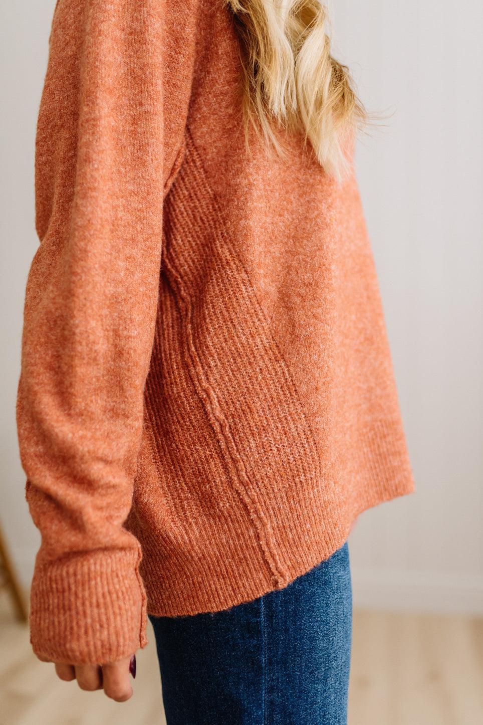 BLONDE WOMAN WEARING A HIGH-LOW HEM, LONG SLEEVE, SUPER SOFT, OVERSIZED CREW NECK SWEATER WITH RIB DETAILS AND STANDING IN A STUDIO WITH LIGHT WOOD FLOOR AND PANELED WALL BEHIND.